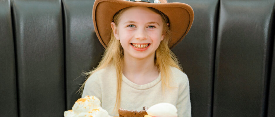 Young girl sitting at dining table and smiling with a platter of desserts in front of her.