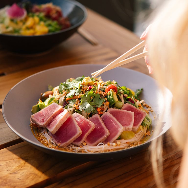 a bowl of noodle salad with fresh greens and tuna on the side