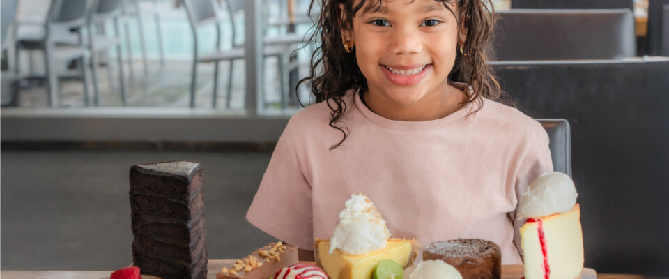 Young girl sitting at a table smiling with a platter of desserts on table.