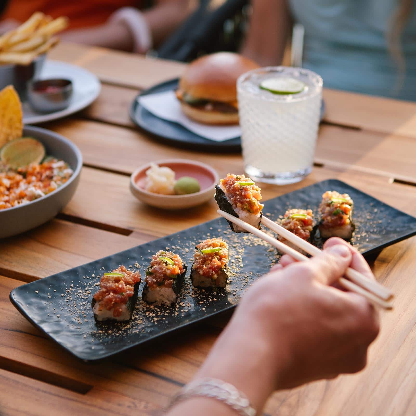 a hand using a pair of chopstick to pick up a tuna temaki sushi roll