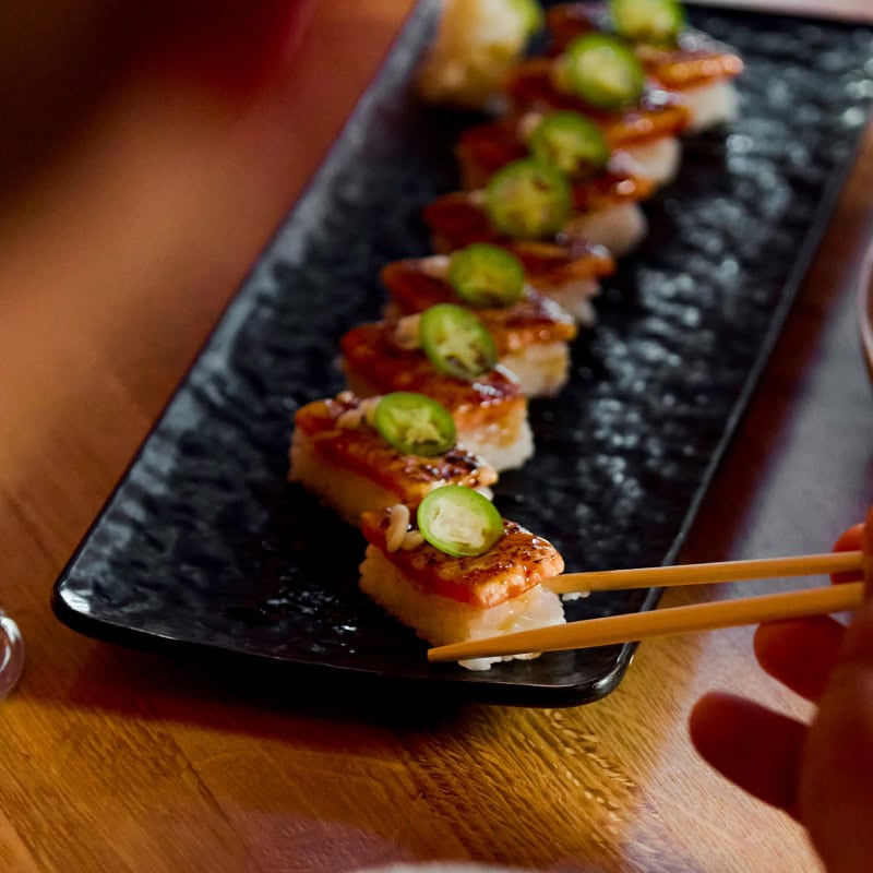 a hand using a pair of chopstick to pick up a tuna temaki sushi roll
